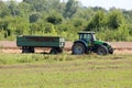 Green and black farm tractor with connected rusted vintage old tractor trailer left in local field Royalty Free Stock Photo