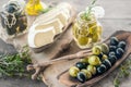 Green and black olives in glass jars with white soft brie cheese and young olives branch on a wooden background, a bottle of olive Royalty Free Stock Photo