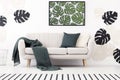 Green blanket and cushion on settee in white living room interior with poster of leaves. Real photo Royalty Free Stock Photo