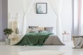 Green blanket thrown on double bed with many pillows and grey sh