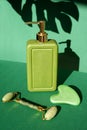 Green bottle with a jade roller massager and gua sha scraper for face massage