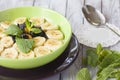 Green bowl of cereal with bananas, prunes and raisins on wood background