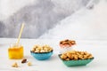 A green bowl of roasted cashews, a blue bowl of peeled hazelnuts, a white bowl of almonds, and a glass jar of honey stand against Royalty Free Stock Photo