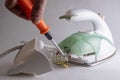 Green broken iron. The wizard`s hand twists the screw with an orange screwdriver. The concept of repair of electrical household