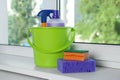 Green bucket with cleaning supplies and sponges on window sill indoors