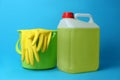 Green bucket with gloves and canister of detergent on light blue background. Cleaning supplies Royalty Free Stock Photo