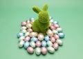 Green bunny, rabbit surrounded by small Easter chocolate eggs, sweets wrapped in colorful Royalty Free Stock Photo