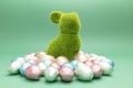 Green bunny, rabbit surrounded by small Easter chocolate eggs, sweets wrapped in colorful