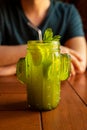 Green cactus shaped glass with Lemonade, lime, mint leaf and drinking straw. Male hands and Cold green tea or cocktail on wood Royalty Free Stock Photo