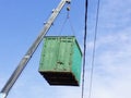 Green cargo container which gray boom with blue hook of truck manipulator lift up near the power line Royalty Free Stock Photo
