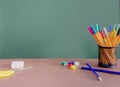 Green chalkboard with space for text behind the desk with colorful pens and pins