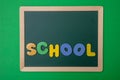 Green chalkboard with wooden frame, word school in colorful letters, green wall background