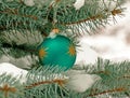 Green Christmas ball hanging on a snow-covered branch of a Christmas tree on a festive background of white snow and snowy bokeh Royalty Free Stock Photo