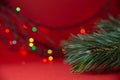 Green Christmas tree branch close-up and bright multicolored lights garlands blurred in bokeh on a red background. Royalty Free Stock Photo