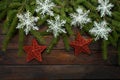 Green Christmas tree branches on a dark wooden background. New Year background with two red stars and white snowflakes. Top view Royalty Free Stock Photo