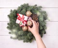 Green Christmas Wreath with Decorations on White Wooden Background Christmas Card Christmas Gift Box Top View Flat Lay Female Hand Royalty Free Stock Photo