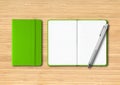 Green closed and open lined notebooks with a pen on wooden background