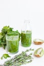 Green cocktail in a bottle and in a glass with spinach, mint, rosemary, kiwi and apple on a light background.