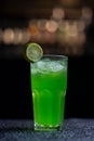 green cocktail with lime garnish in a tall glass