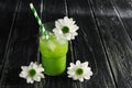 A green cocktail with striped straws is decorated with white flowers. Kiwi juice with ice on a wooden black table. Place for your