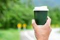 Green coffee cup take away in hand with blurred road backgro