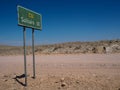 Green color directional road sign pole along unpaved dirt road C14 to Solitaire among rock desert landscape with blue sky