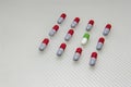 Green colors odd capsule amongst red capsules on white background.