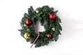 Green coniferous Christmas wreath decorated with red and yellow Christmas balls with bells and one candy can in the center on a wh Royalty Free Stock Photo