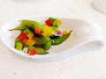 Green cooked lima beans with yellow and red peppers , onion in a white spoon