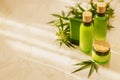 Green cosmetic bottles with wooden caps and hemp leaf on marble surface