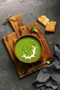 Green cream broccoli soup with sour cream and pumpkin seeds in a ceramic bowl on a cutting board, dark rustic background. View Royalty Free Stock Photo