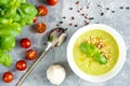 Green cream soup on the white bolw, spoon, garlic, cherry tomatoes, black and red grainy pepper, grey background Royalty Free Stock Photo