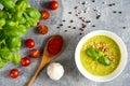 Green cream soup on the white bowl, basil, cherry tomatoes, wooden spoon with red pepper, garlic Royalty Free Stock Photo