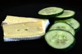 Green cucumber and brie cheese slices isolated on black shiny plate Royalty Free Stock Photo