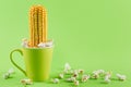 Green cup on a green background, popcorn is scattered around, an ear of corn sticks out of the cup, as a symbol, concept Royalty Free Stock Photo