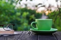 Green cup of hot coffee and glasses with a book and newspaper on a wooden table in the garden in the morning or evening. Summer Royalty Free Stock Photo