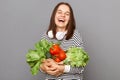 Green diet, healthy living. Laughing woman holding vegetables isolated over gray background. Vegetarian lifestyle, health choice. Royalty Free Stock Photo