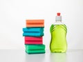 Green dishwashing gel and a set of sponges on a white table.