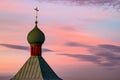 The green dome of the church with a cross on a pink and blue morning sky. The dome of the church is made of green metal