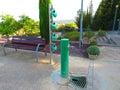 Green drinking park fountain with set of four green plastic watering cans and wooden benches bottom for sitting Royalty Free Stock Photo