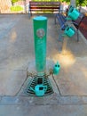 Green drinking park fountain with set of four green plastic watering cans and wooden benches bottom for sitting Royalty Free Stock Photo