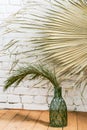 Green dry branch of home date palm in beautiful glass bottle of blue glass on background of white brick wall Royalty Free Stock Photo