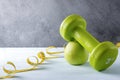 Green dumbbell, Apple, yellow measuring tape on a gray background