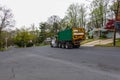 A green dumpster is being transported on the bed of a heavy duty truck on a street in a residential community.