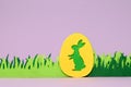 Green easter egg with yellow bunny and fabric green handmade grass on a light purple background. Easter greeting card with green Royalty Free Stock Photo