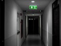 Green exit fire sign hanging on ceiling on dark mysterious corridor in building near fire exit door Royalty Free Stock Photo