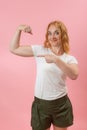 Green Eyes young woman showing muscles . Side view portrait lovely powerful cheerful red hair gerl on pink pastel background