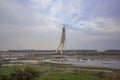 Green farm fields near a cable-stayed bridge under construction and a tower crane over the Yamuna River against a blue sky. Royalty Free Stock Photo