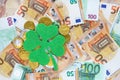 Green felt four leaf clover placed on chocolate euro cents coins, euro banknotes background. Saint Patricks day.