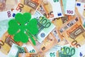 Green felt four leaf clover on surface covered with 50 and 100 euro banknotes, on the left side.